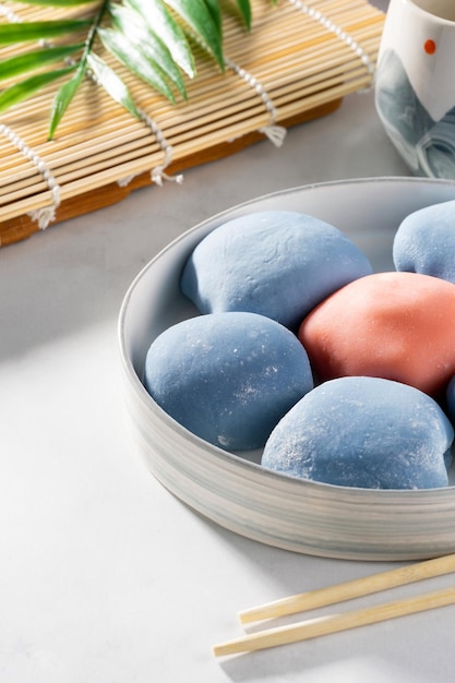 A ceramic bowl of Japanese mochi with chopsticks and maki sudare mat on white countertop Concept of a traditional Japanese dessert Asian rice cake mochi ice cream sweet street food