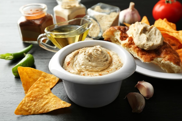 Ceramic bowl of tasty hummus with chips and flat bread on table