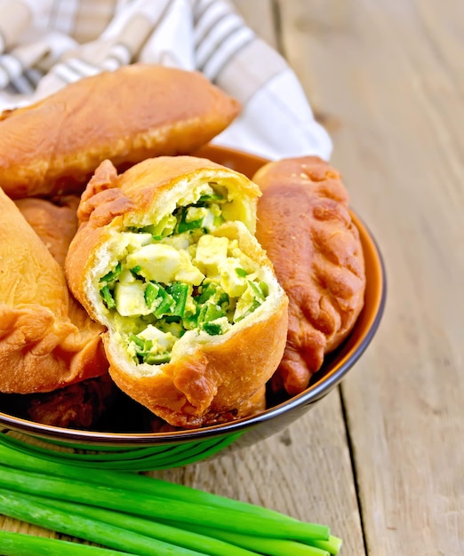 Ceramic bowl with fried patties with onion and egg napkin bunch green onions on a wooden boards background