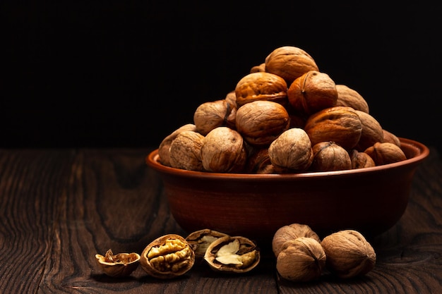 ceramic bowl with nuts on wooden table and black background