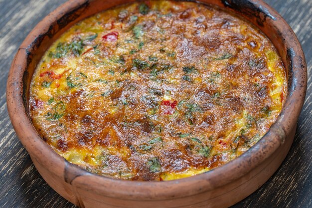 Ceramic bowl with vegetable frittata, simple vegetarian food. Frittata with tomato, pepper, onion and cheese on wooden table, close up. Italian egg omelette, top view