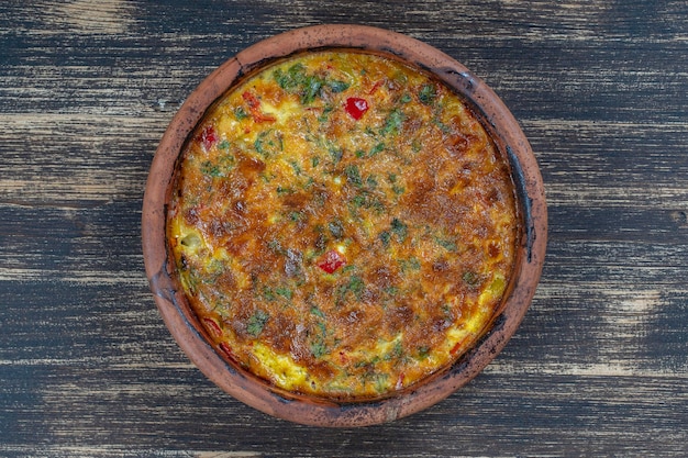 Ceramic bowl with vegetable frittata simple vegetarian food Frittata with tomato pepper onion and cheese on wooden table close up Italian egg omelette top view