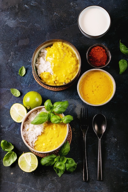 Ceramic bowl of yellow curry served with basil and limes