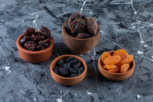 Photo ceramic bowls of tasty dried fruits on marble surface.