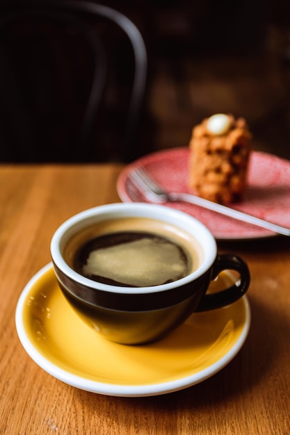 A ceramic cup of black coffee and a dessert served on a plate on the wooden table in a cafe a closeup