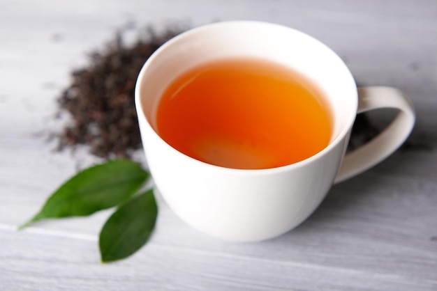 Ceramic cup of tea with scattered tea leaves around on light wooden background