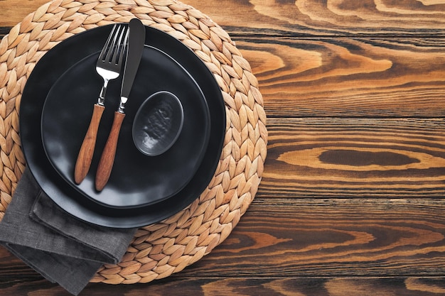 Ceramic empty black plate silverware and linen kitchen towel\
napkin on old brawn wooden table background cooking stone backdrop\
top view with copy space flat lay