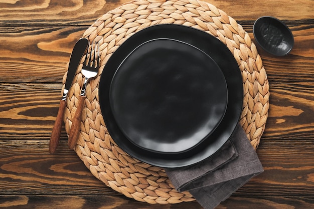 Ceramic empty black plate silverware and linen kitchen towel
napkin on old brawn wooden table background cooking stone backdrop
top view with copy space flat lay