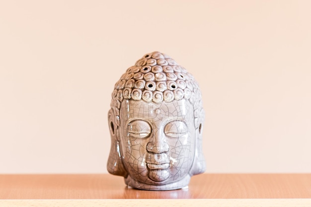 Ceramic figurine of buddha head on beige background.