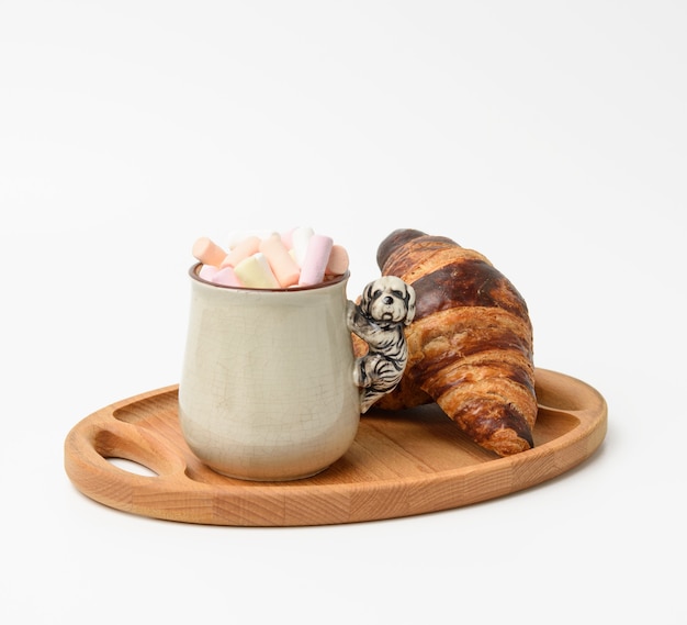 Ceramic mug with cocoa and marshmallows, baked croissant on a wooden serving plate, food on white background