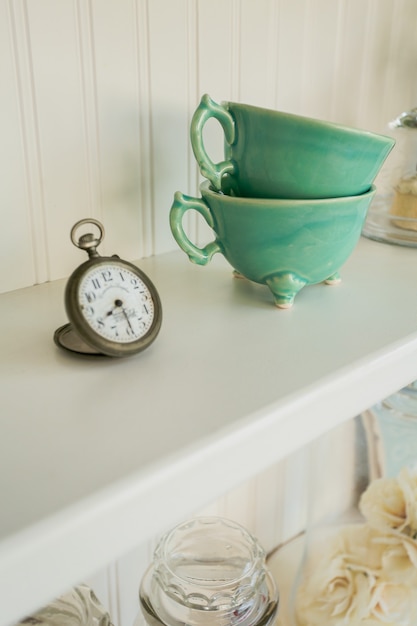 Ceramic mugs and decorative pocket watch on a kitchen shelf