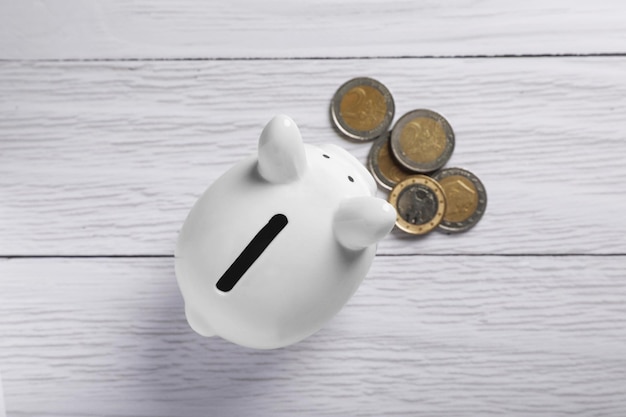 Ceramic piggy bank and coins on white wooden table flat lay Financial savings