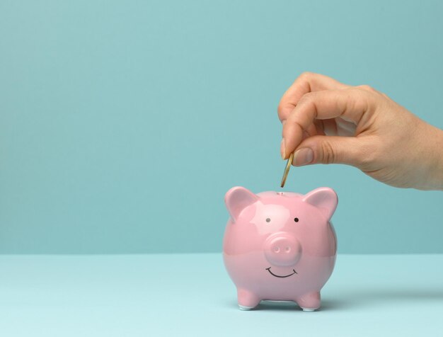 Photo ceramic pink piggy bank and hand throwing a coin inside finance savings concept