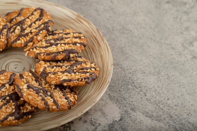 Ceramic plate of glazed oatmeal biscuits on stone table.