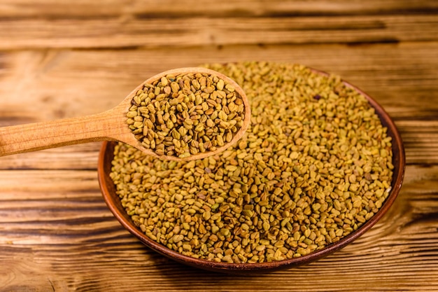 Ceramic plate and spoon with fenugreek seeds on wooden table