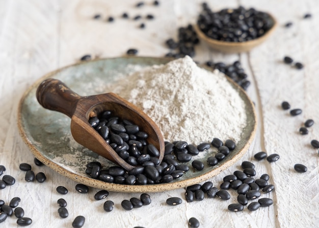 Ceramic plate with black beans flour and dried beans with a wooden spoon closeup. Healthy eating and vegetarian concept. Traditional Latin American cousin ingredient