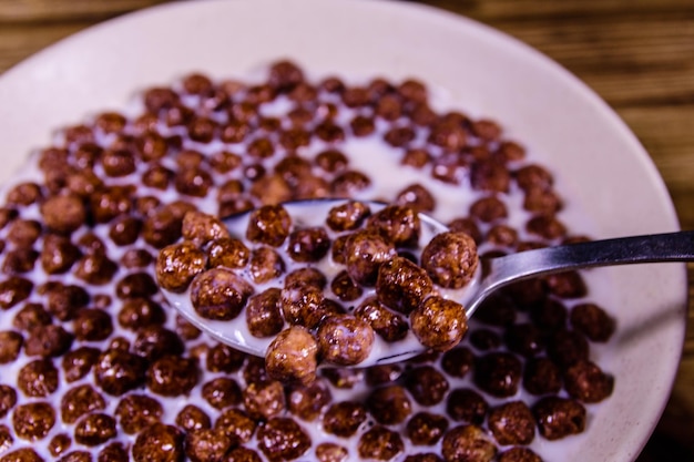 Ceramic plate with chocolate cereal balls in milk on rustic wooden table