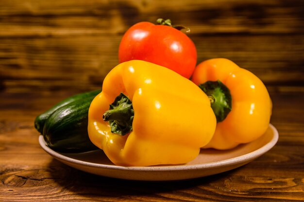 Ceramic plate with cucumbers tomatoes and sweet pepper on wooden table