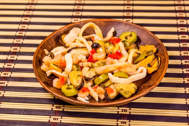 Ceramic plate with different sea food and olives on a bamboo mat