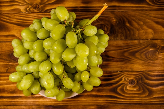 Ceramic plate with green grapes on wooden table Top view