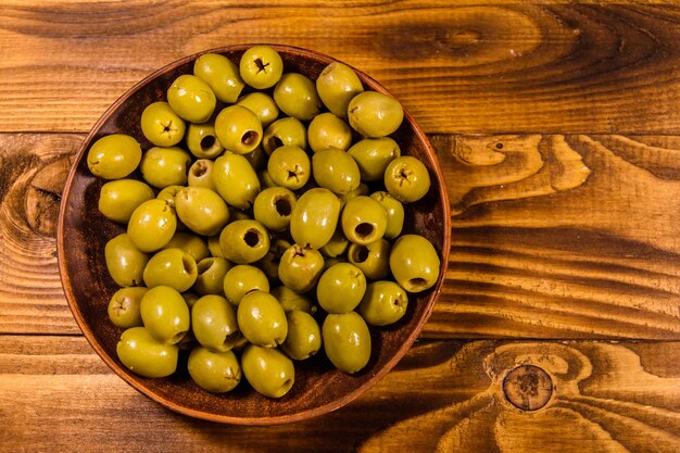 Ceramic plate with green olives on wooden table Top view