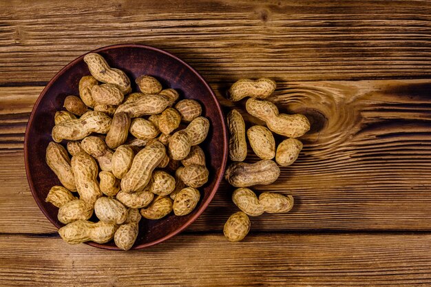 Ceramic plate with heap of the unpeeled peanuts on a wooden table. Top view