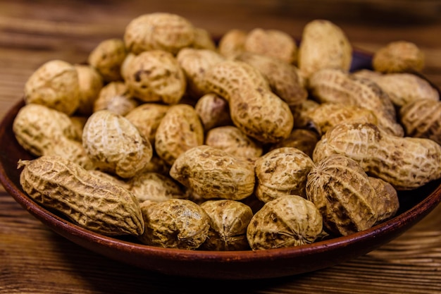 Ceramic plate with heap of the unpeeled peanuts on a wooden table