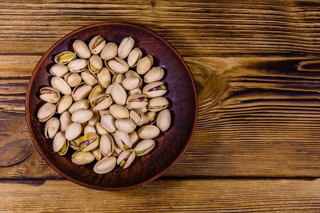 Ceramic plate with pistachio nuts on a wooden table Top view