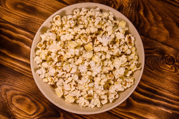 Ceramic plate with popcorn on wooden table Top view