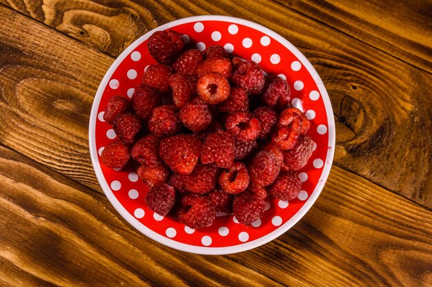 Ceramic plate with ripe raspberries on rustic wooden table Top view