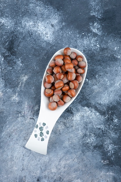 Ceramic spoon of shelled organic hazelnuts on marble.