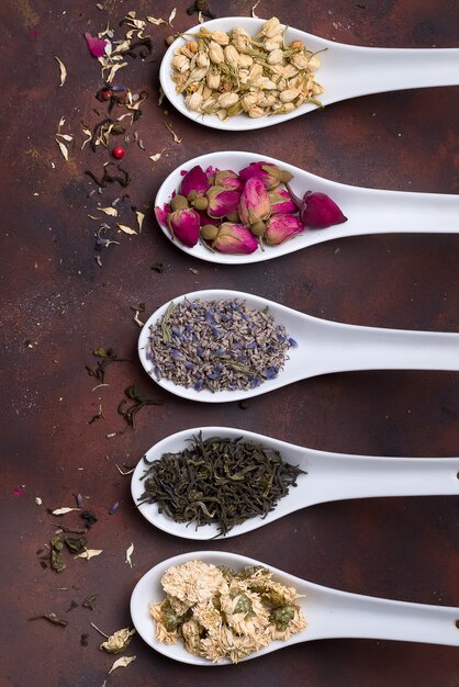 Ceramic spoons with dried herbs, flower buds and tea leaves over stone background