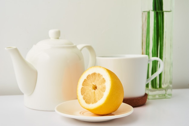 Ceramic teapot cup of tea with lemon and flowers in vase on white background kitchen interior tea time concept