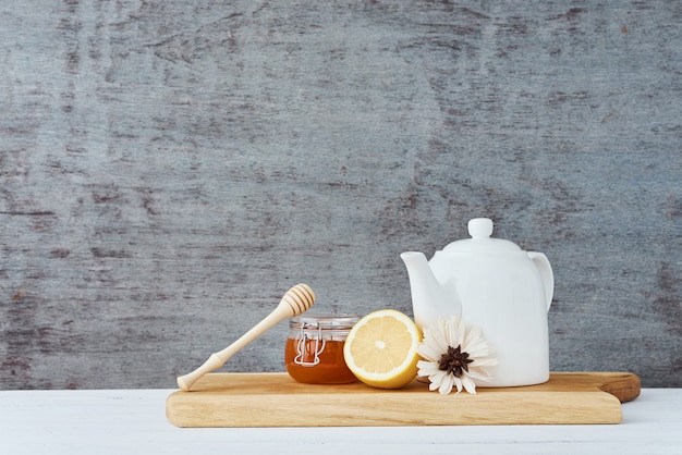 Ceramic teapot, white cup, honey in a glass jar and lemon on wooden 