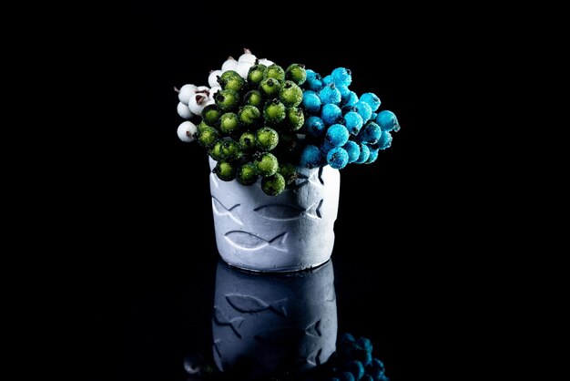 Ceramic vase with fishes with blue white and red berries in ice with reflection black background isolated