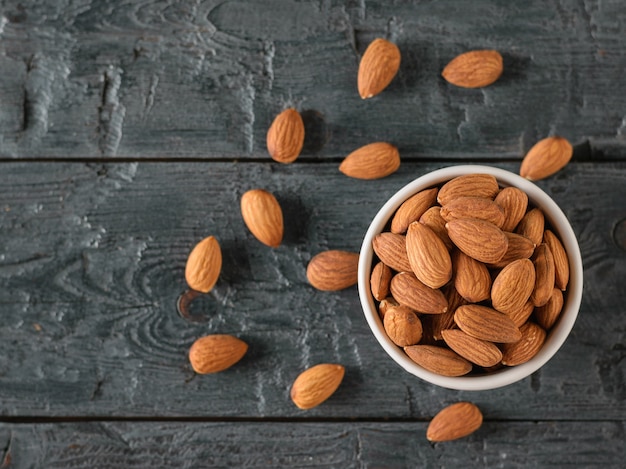 Ceramic white Cup with almonds on black wooden rustic table. Vegetarian food. Flat lay. The view from the top.