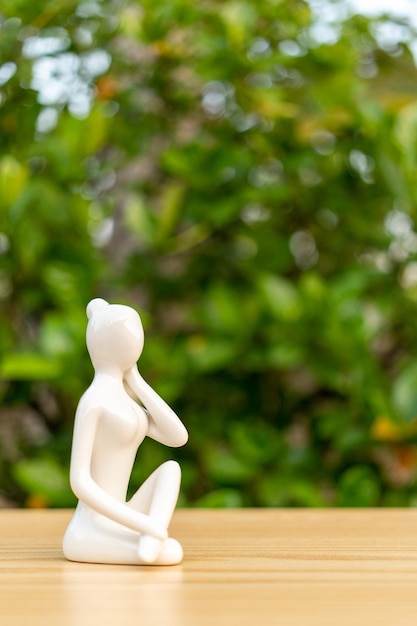 Керамическая статуэтка йоги женщины, занимающейся йогой, на деревянном полу и фоне зеленых листьев