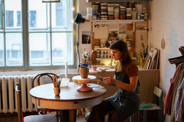 Фото Керамист в вазе лепки фартука на мастер-классе в студии владелец студии керамики молодой женщины на работе