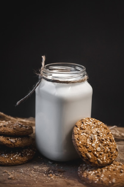 Biscotti ai cereali con una brocca di latte su uno sfondo di legno.