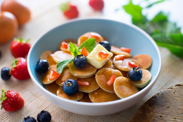 Cereal Mini pancakes with butter and red fruits in a bowl.