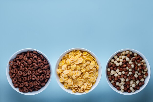 Photo cereals bowl with chocolate balls, rings and yellow corn flakes for dry breakfast on blue surfce. copy space, top view