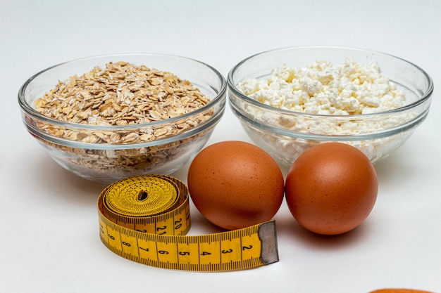 Cereali, nastro di misurazione, ricotta dell'azienda agricola, alto vicino dell'uovo su fondo bianco. concetto senza grassi di dieta sana della proteina.