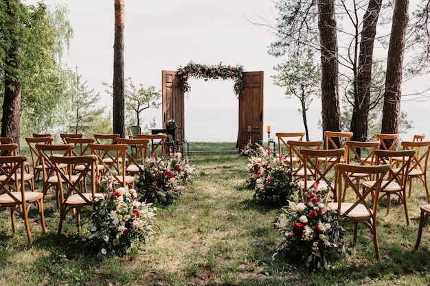 Ceremonie, boog, huwelijksboog, huwelijk, huwelijksmoment, decoraties, decor, huwelijksdecoraties, bloemen, stoelen, buitenceremonie in de open lucht, boeketten bloemen.