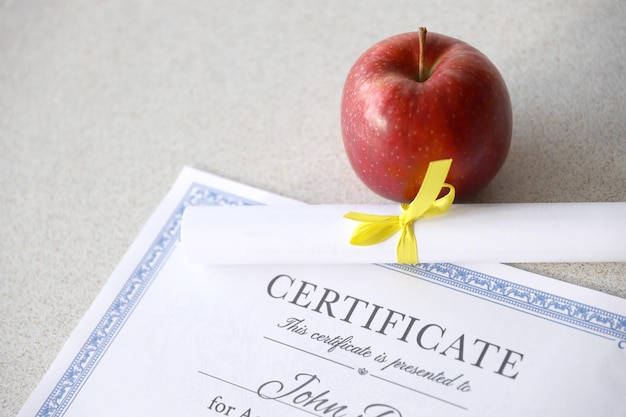 A certificate of achievement lies on table with small scroll and red apple Education documents