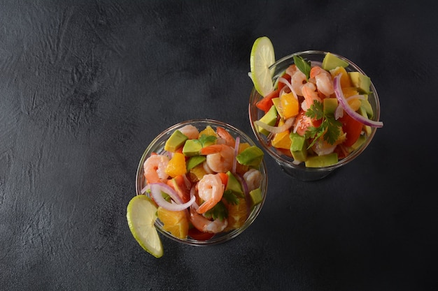 Cevichesalade met garnalen, sinaasappelen en avocado in glazen kom op een donkere of grijze achtergrond. Latijns-Amerikaans eten. Heerlijke, vers gemaakte garnalenceviche. Garnalen gemarineerd in limoen en sinaasappel.