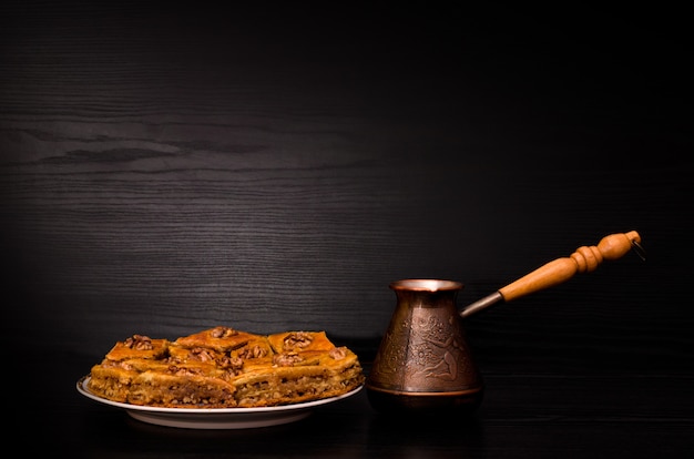 Cezve van koffie en een plaat van baklava met honing op zwart