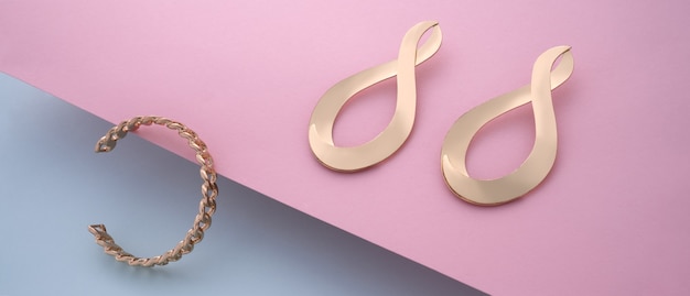 Chain shape golden bracelet and modern earrings pair on pink and blue