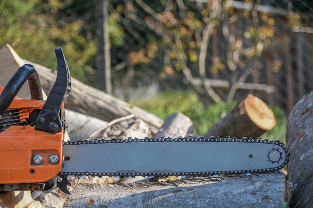 Photo chainsaw that stands on a heap of firewood in the yard on a background of firewood and trees cut by a chainsaw.