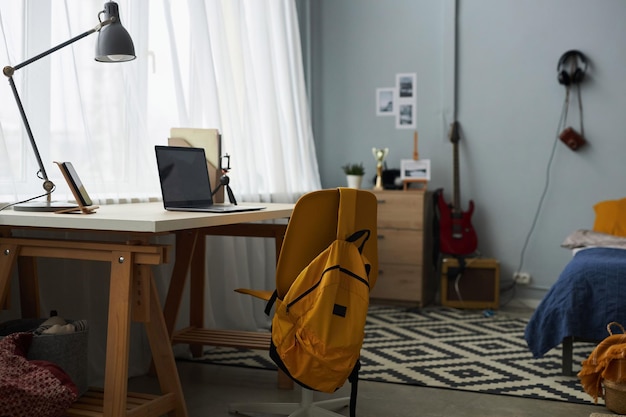 Chair with yellow backpack standing in front of desk with lamp and laptop