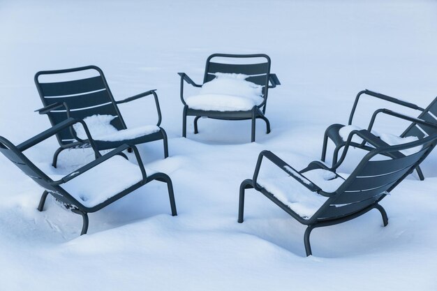 白い雪の厚い層で覆われた公園の屋外の椅子 冬の天気の間の金属製の庭の家具 吹雪の後の屋外の家具 通りのレストランの椅子